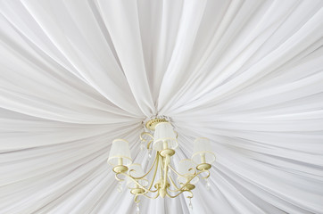 Classic chandelier hanging on ceiling made of white cloth. View from bottom.