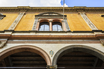 A yellow building facade with a renaissance type architecture full of ornaments, with two archs and...