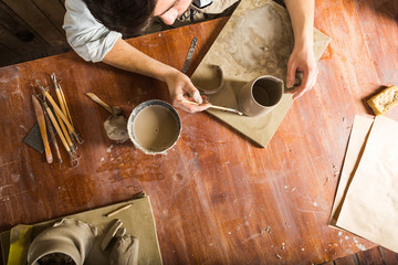 pottery, stoneware, ceramics art concept - workplace of potter, craftsman bent over clay cup with...