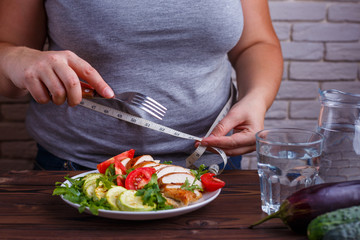 Dieting, healthy low calorie food, weight losing concept. Overweight woman with measuring tape on her waist eating salad from a bowl