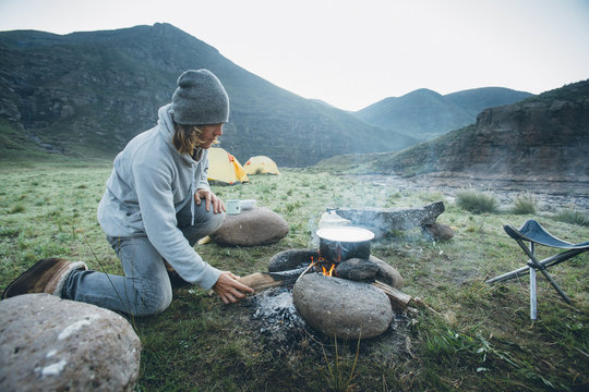 outdoorsman stoking a cooking fire whilst camping in the mountains