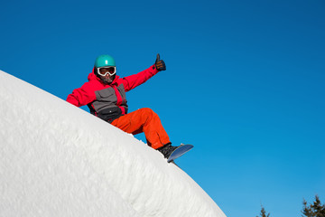 Fototapeta na wymiar Shot of a happy snowboarder sitting in the snow on top of the mountain showing thumbs up