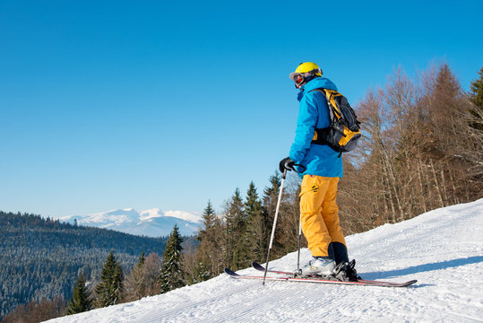 Full length shot of a skier wearing colorful winter sportswear standing on the slope enjoying beautiful view while skiing in the mountains copyspace active hobby lifestyle concept