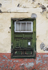 Fototapeta na wymiar green old shabby window in a decaying house with weathered wood and peeling paint set in a yellow flaking concrete wall