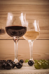 Red and white wine glasses and grape on wooden table