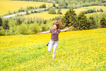 Fototapeta premium Young woman running, jumping in air and smiling on countryside yellow dandelion flower fields in summer grass in Ile D'Orleans, Quebec, Canada smiling