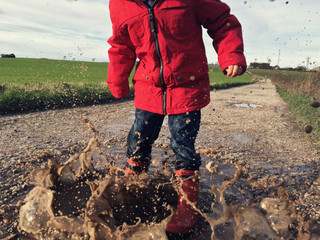 Child jumping in a muddy puddle
