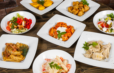 Set of different salads, dumplings and ravioli on a wooden table