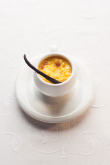 Creme brulee with vanilla pod in white cup, on whitw tablecloth.