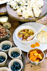 housemade, meal, dessert concept. table setting with numbers of such treats as nuts, berries, dried apricots, nearby with little dish of honey and homemade bread