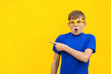 Look this! Handsome young child in shoked. Pointing away while standing isolated on light yellow background