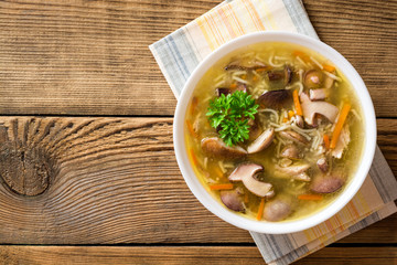 Chicken soup with mushrooms and noodles on rustic wooden table