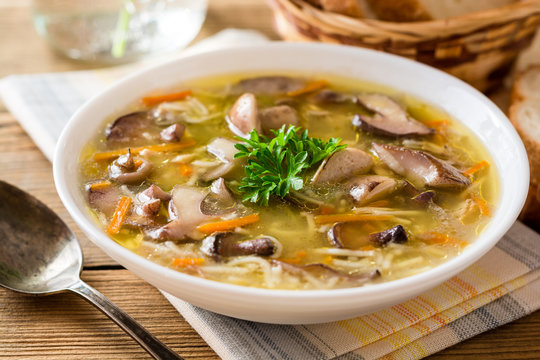Chicken soup with mushrooms and noodles on rustic wooden table