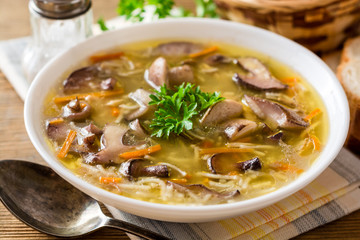 Chicken soup with mushrooms and noodles on rustic wooden table