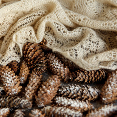 Winter holidays background of pine cones powdered with artificial snow and white downy shawl. Merry Christmas brown backdrop.