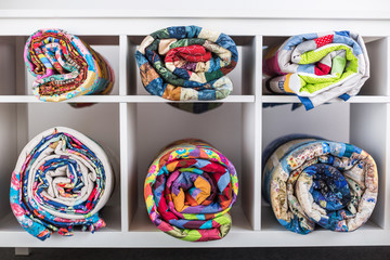 patchwork, sewing, tailoring and fashion concept - bright finished quilts in the studio or in the shop, white shelves with six storage compartments with goods, the warehouse of finished products