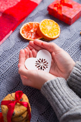 Female hands in gray knitted sweater holding heart on Christmas decorative background