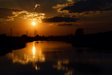 Fototapeta premium Orange Sunset By The River With Reflections And Silhouettes Of Industrial Area