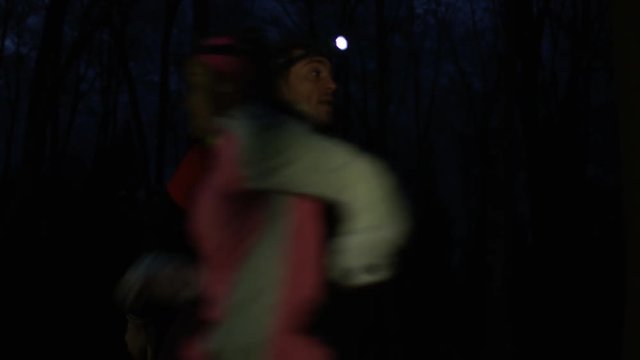 Endurance training group running in the woods at night, wearing lamps on headgear.