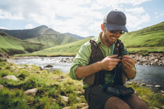 fly fisherman sitting near a river tying a fly