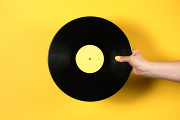 Hand holding vinyl record over yellow background
