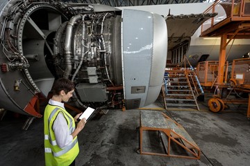 Female aircraft maintenance engineer examining turbine engine of