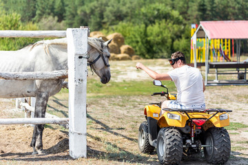 Obraz premium Caucasian man on ATV quad bike meet beautiful white horse on a farm or ranch. Evolution of vehicles for centuries concept. Past and present progress