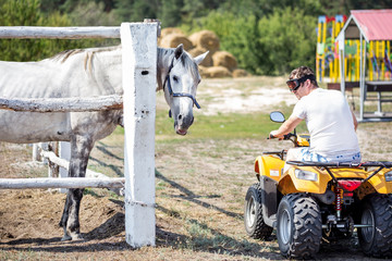Obraz premium Caucasian man on ATV quad bike meet beautiful white horse on a farm or ranch. Evolution of vehicles for centuries concept. Past and present progress