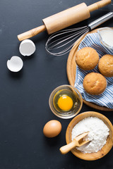 Baking ingredients. Bowl, eggs, flour, eggbeater, rolling pin and eggshells on black chalkboard from above.