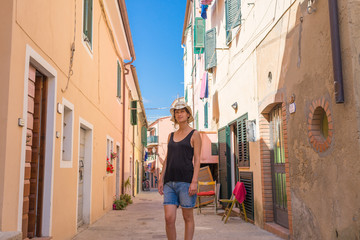 Fototapeta na wymiar Italian summer holidays: woman standing alone in a colorful alley narrow street in an old village in Sicily, Italy