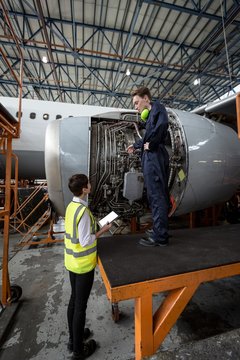 Male aircraft maintenance engineers examining turbine engine of