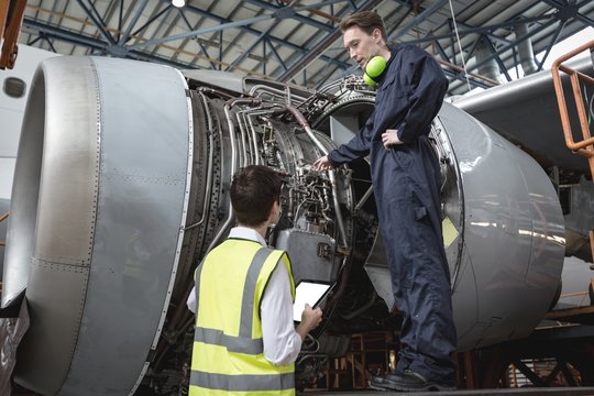 Male aircraft maintenance engineers examining turbine engine of
