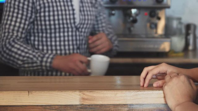 Barista is finishing making coffee. He gives it to the customer. The woman starts drinking her drink. A woman comes to the cafe