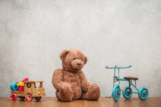 Retro Teddy Bear, old toy tricycle and obsolete classic wooden truck with construction blocks front concrete textured wall background. Vintage instagram style filtered photo