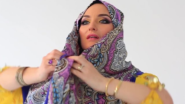 Beautiful arabian girl in black and yellow national clothing, covering her head in white studio backgraund . Slow motion