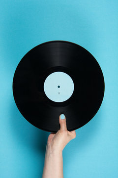 Hand holding vinyl record over blue background
