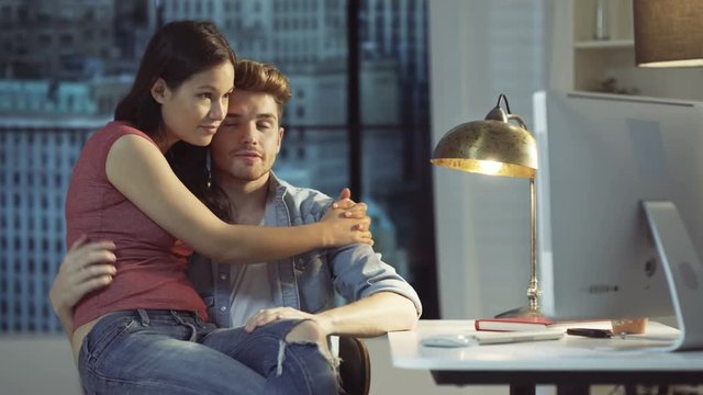  Affectionate couple chatting & using computer together in city apartment