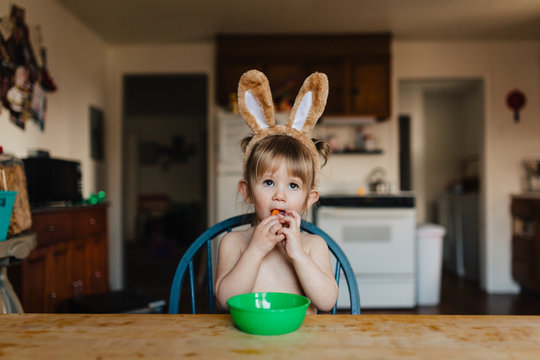 Toddler child eating baby carrots while wearing bunny ears.