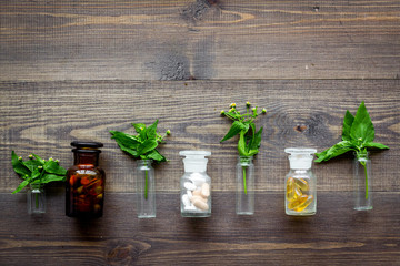 Herbal medicine pattern. Leaves, bottles and pills on wooden background top view copyspace