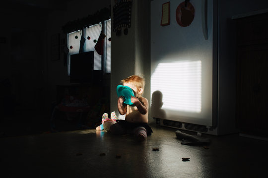 Toddler holding bowl in face sitting in sunlight 