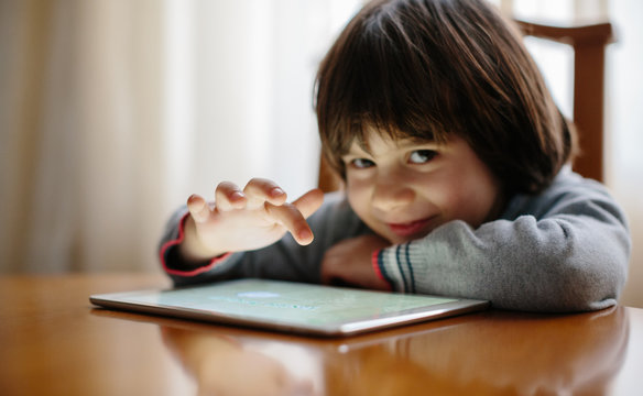 Small boy smiling at camera while using a digital tablet