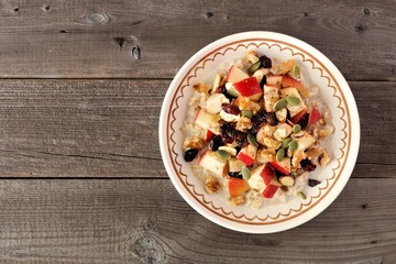Healthy autumn breakfast oatmeal with apples, cranberries, seed and nuts, overhead view on wood