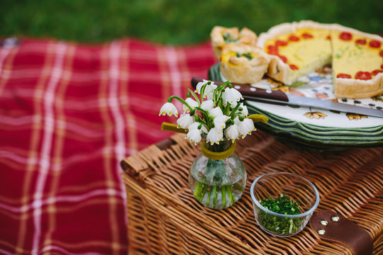 snowdrops on wooden picnic basket with a sliced vegetarian quiche in the back