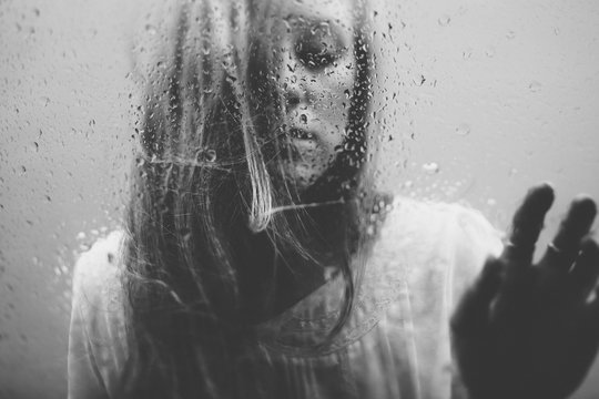young blonde woman standing behind glass with rain drops