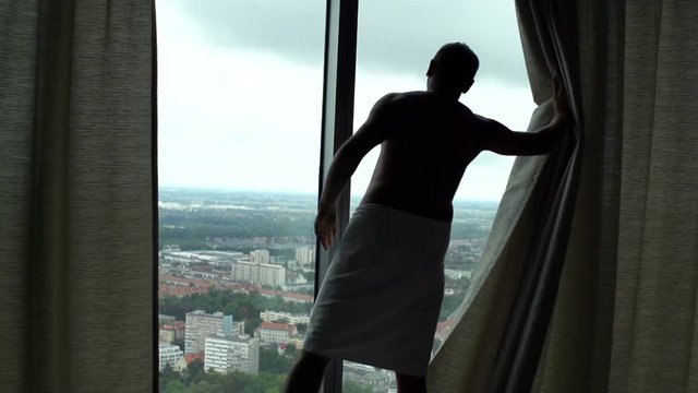 Man in towel unveil curtains and admire view from window at home, super slow motion 240fps
