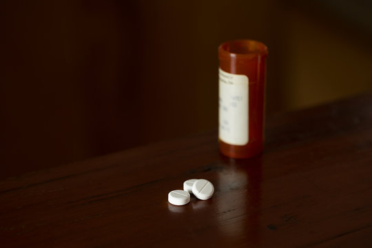 Prescription painkillers, oxycodone, lying on a wooden table with prescription medication bottle in the background.