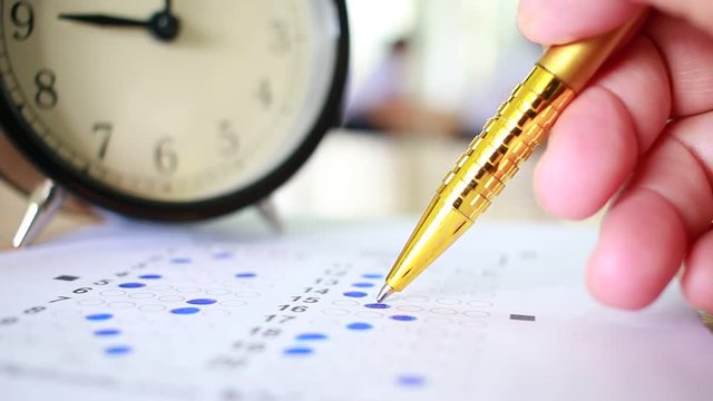 Asian Students taking optical form of standardized exams near Alarm clock with hand holding yellow pen for final examination in secondary school, college university classroom, Education concept