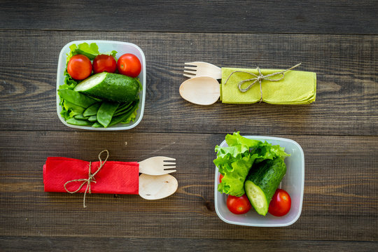 Healthy meal in containers. Salad with tomato and cucumber in cotainers on wooden background top view