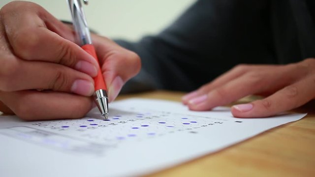Asian Students holding pencil in hand doing multiple-choice quizzes or testing exams answer sheets exercises on old wood table In blur student school, college university classroom in education concept