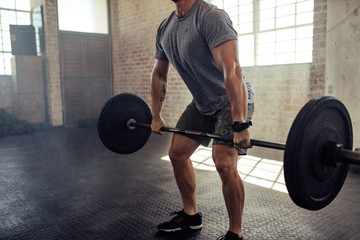 Muscular young man lifting barbell at gym